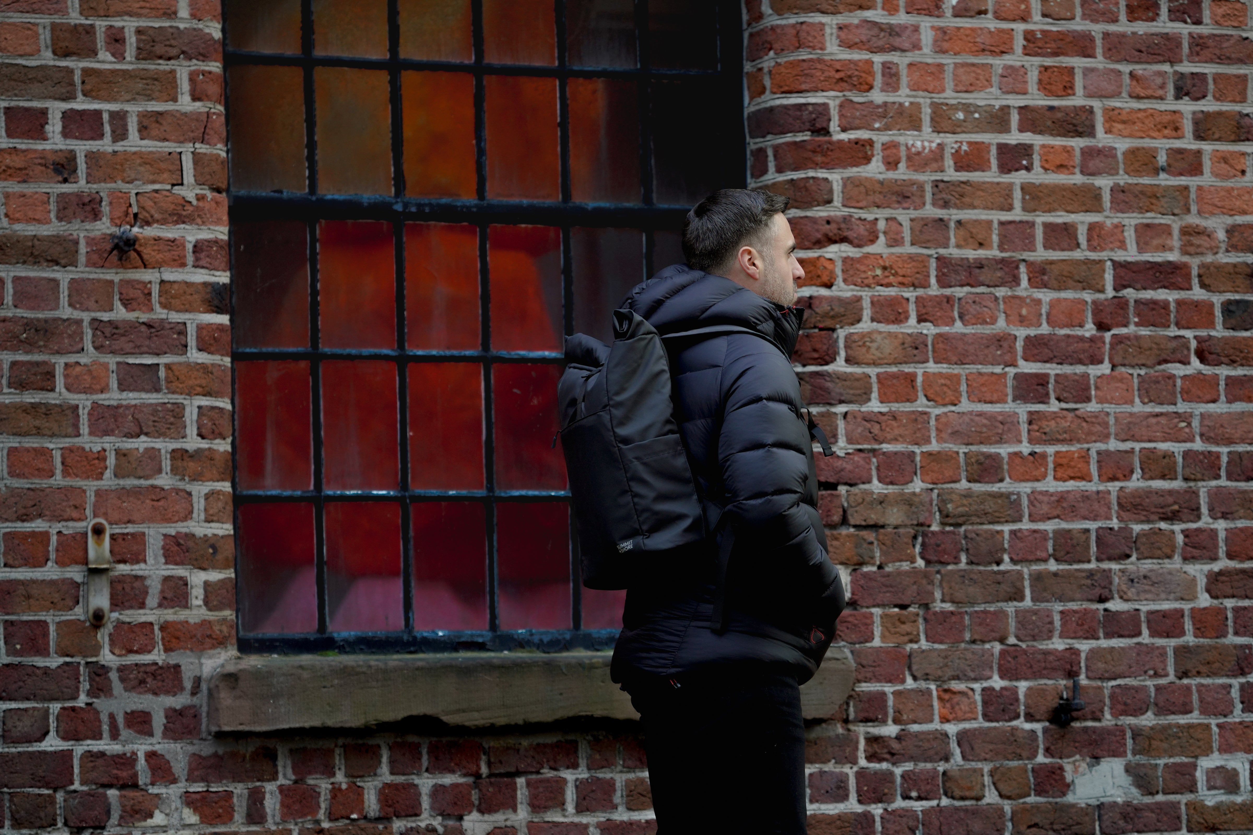 All Black Outfit with Summit and Shore Roll Top Backpack by Window with Coloured Reflections