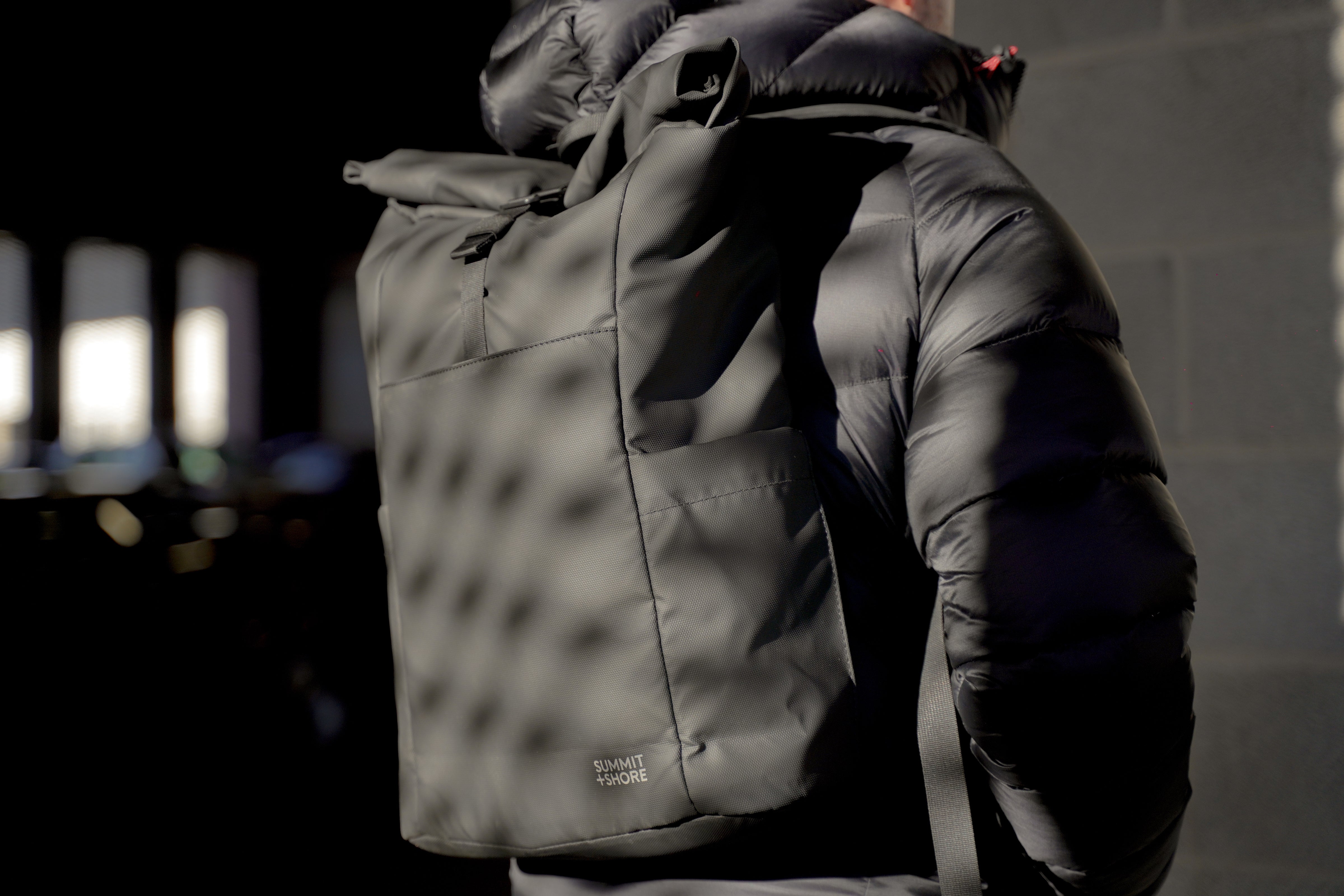 Close Up of Summit and Shore Roll Top Backpack Worn By Man in Dappled Sunlight