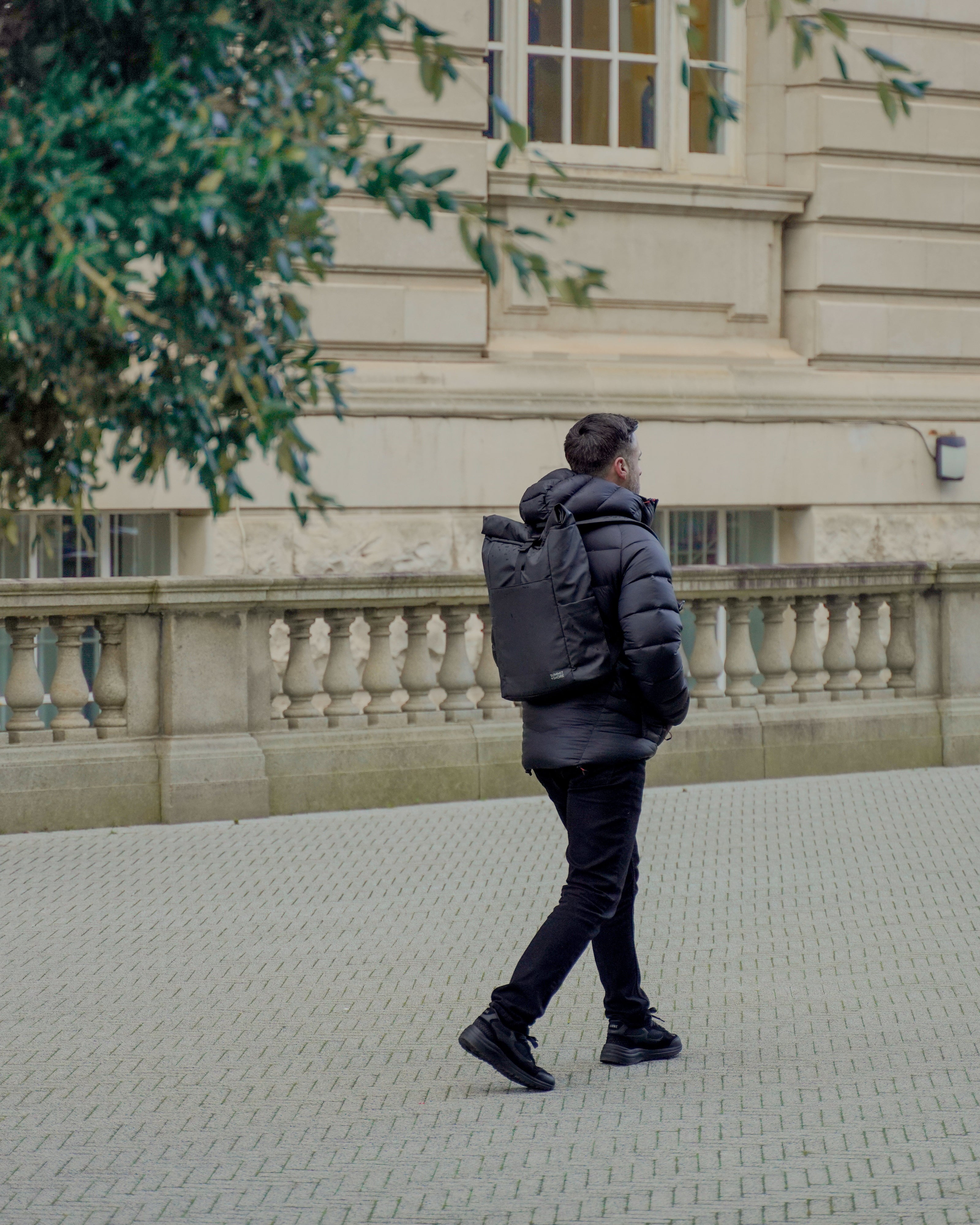 Man Walking Through Leafy City with Summit and Shore Roll Top Backpack